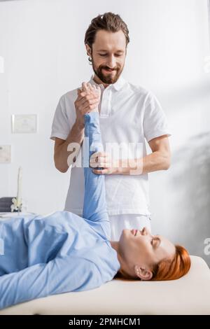 Lächelnder Physiotherapeut streckt den Arm der Frau während der Schmerzlinderung Massage in der Genesungseinrichtung, Stammbild Stockfoto