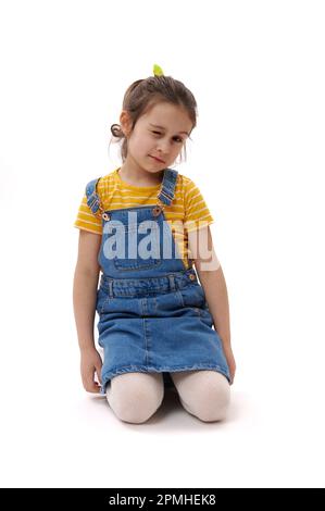 Kaukasische, reizende kleine Tochter, die auf ihren Knien auf einem isolierten weißen Hintergrund sitzt Stockfoto