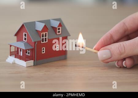 Hand einer Frau mit brennendem Streichholz in der Nähe eines zweistöckigen Hauses Stockfoto