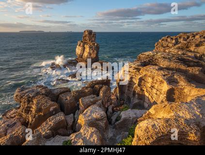 Wellen schlagen gegen Felsgestein in Cabo Carvoeiro im Abendsonnenlicht mit Ilha da Berlenga in der Ferne, Peniche, Centro Region Stockfoto