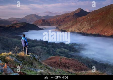 Walker blickt auf den Gipfel von Yr Aran und ein Nebel füllte Nant Gwynant Valley, Nant Gwynant, Eryri, Snowdonia National Park, North Wales, United Ki Stockfoto