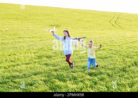 Ein Junge und ein Mädchen, die zwei gelbe und blaue Flugzeuge halten, spielen während des sonnigen Sommertages auf dem Feld Stockfoto