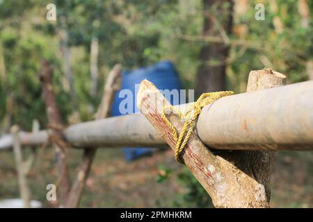 Das Aluminiumrohr, das Wasser transportiert, wird von einem Holzstab und einem Seil getragen Stockfoto