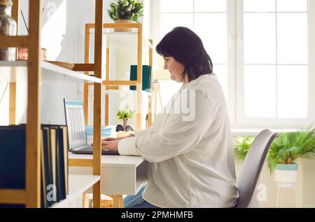 Übergewichtige brünette Frau, die mit einem Laptop im Büro arbeitet Stockfoto