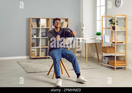 Junger, fröhlicher, lächelnder indianer, der das Lenkrad zu Hause auf einem Stuhl sitzt. Stockfoto