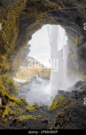 Kvernufoss Wasserfall auf dem Fluss Kverna, von innen gesehen von einer kleinen Höhle hinter dem rauschenden Wasser im Winter, Skógar, Rangárþing Eystra, Süd-Island Stockfoto