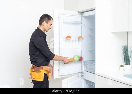 Männlicher Techniker repariert kaputten Kühlschrank in der Küche Stockfoto