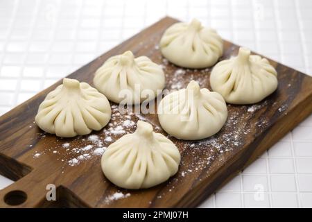 Hausgemachtes ungekochtes Khinkali auf einem Schneidebrett für Olivenholz, georgische Knödel Stockfoto