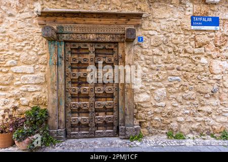 Eine kunstvoll geschnitzte, alte Holztür mit rautenförmigen Zierbeschlägen sitzt in einer Natursteinmauer in der Tayfalar Sokak in der Altstadt von Kyrenia (türkisch: Girne), TRNK. Stockfoto
