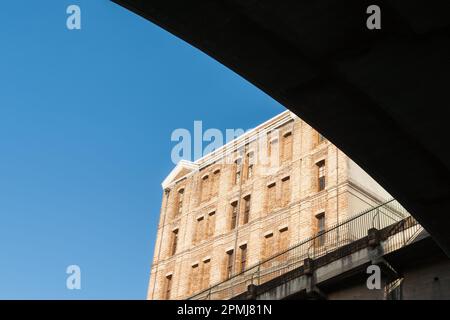 Das Äußere des Backsteingebäudes erhebt sich über den geschwungenen Silhouettenlinien der Unterseite von gegen die blaue Himmelsbrücke Stockfoto