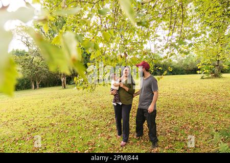 Glückliche lateinische Familie. Mutter und Vater lächelten und sahen ihr kleines Mädchen an, wie es einen Spaziergang unter freiem Himmel machte. Das Konzept eines gesunden Lebensstils Stockfoto