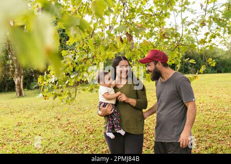 Glückliche Familie einer lächelnden Mutter und eines lächelnden Vaters, die ihre Tochter draußen anschauen. Konzept von Glück, Liebe und Familieneinheit. Stockfoto