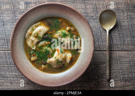 Pilzsuppenteller mit Porcini-Pilzen, Knödeln, Kartoffeln, Karotten, Zwiebeln, Frischer grüner Dill und Pfeffer auf schwarzem Hintergrund, Nahaufnahme, Draufsicht Stockfoto