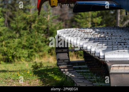 Metallraupen eines Schneepflugs in einem Lagerhaus an einem sonnigen Tag auf einem Sommergelände. Nahaufnahme eines speziellen Schneemobils mit Raupe im Karpaten Stockfoto