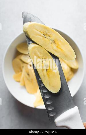 Hand schneidet Mehlbananen, schneidet gelbe Mehlbananen zum Braten, Verfahren zur Herstellung gebratener Mehlbananen Stockfoto