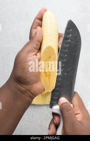 Hand schneidet Mehlbananen, schneidet gelbe Mehlbananen zum Braten, Verfahren zur Herstellung gebratener Mehlbananen Stockfoto