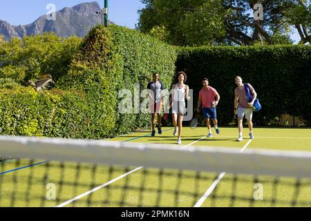 Glückliche, vielfältige Gruppe von Freunden, die zusammen auf dem Tennisplatz ankommen Stockfoto