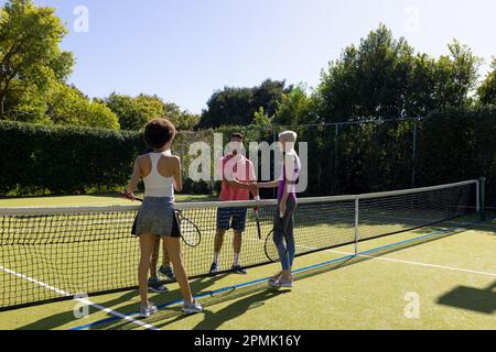 Glückliche, vielfältige Gruppe von Freunden, die Tennis spielen, sich auf dem Tennisplatz die Hand schütteln Stockfoto