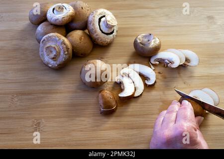 Schneiden von Kastanienpilzen auf einem Holzbrett Stockfoto