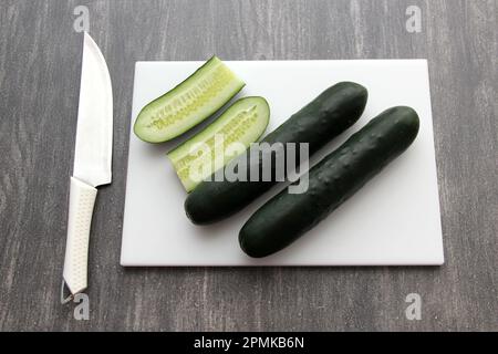 Frische, grüne Gurken auf einem Schneidebrett mit Messer werden für einen nahrhaften Salat oder Saft auf einem Küchentisch zubereitet Stockfoto