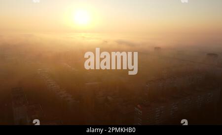 Sonnenaufgang in der Stadt. Helle Sonne bei Sonnenaufgang, Nebel über den Dächern der mehrstöckigen Gebäude. Blick von oben auf viele Häuser und die Stadt. Panoramablick auf die Landschaft. Stadtbild, Stadtlandschaft. Draufsicht Stockfoto
