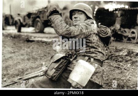 World war Two B&W Foto Ein deutscher Soldat macht während der Ardennenoffensive 1945 Fortschritte . Der Mann ist aus der 1. SS Panzer Division, gekleidet in einer Dot Camo Jacke, bewaffnet mit einem Angriffsgewehr Stg44 Stockfoto