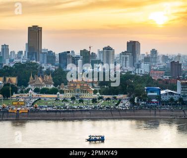 Blick auf das Dach, Blick auf die Flussgegend von Kambodschas Hauptstadt. Sonnenuntergang über dem Königspalast und den Hochhäusern dahinter, als kleines Boot Stockfoto