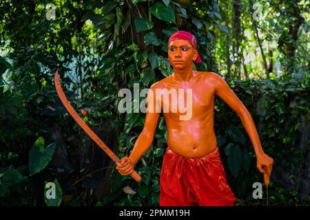 Porträt eines Hindu-Anhängers, der am letzten Tag des Bangla-Monats am Stadtrand von Dhaka in Munshigonj an einem Festival namens Lal Kach (Rotes Glas) teilnimmt. Das Festival ist der Verehrung von Lord Shiva und Parvati gewidmet. Es wird angenommen, dass eine Gruppe von Soldaten unter Shiva auf der Erde auftaucht, mit der Mission, die Mächte des Bösen abzuwehren. Diese Soldaten, die im göttlichen Licht Shivas leuchten, marschieren zu nahe gelegenen Tempeln. Das alles ist Teil einer sehr langen Tradition, die Hunderte von Jahren zurückreicht. Die Hindus, vor allem die Jungen, malen sich rot an, nehmen Schwerter und holen Prozessi heraus Stockfoto