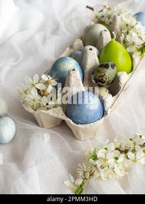 Blau bemalte ostereier und Kerze im Tablett. Gefärbte Ostereier mit Marmoreffekt, hellblaue Farbe auf weißer Tischdecke und Kirschblüte. Eier Backgr Stockfoto