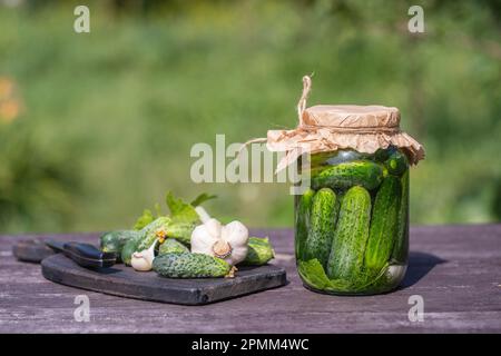 Frisch und gesalzen, eingelegte grüne Gurken in einem Glasgefäß auf einem alten Holztisch im Sommergarten an sonnigen Tagen, Kopierbereich, Nahaufnahme. Glas mit grieß Stockfoto