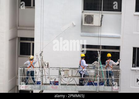 Der Maler verwendet einen langen Stock, um die Wand hoch oben zu malen, ein riskantes Werk, während er Arbeiten in der Luft aufhält. HDB-Gebäude, das von der Regierung gebaut wurde. Singapur. Stockfoto