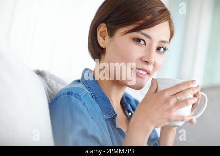 Es gibt nichts Schöneres als die erste Tasse Kaffee... eine attraktive asiatische Frau, die eine Tasse Kaffee genießt. Stockfoto