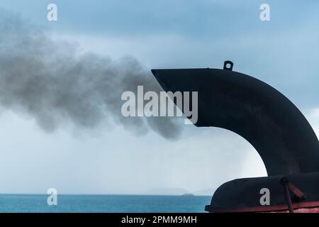 Rauch aus dem Fährboot im Hintergrund, aus der Nähe, Thailand. Schornstein einer Fähre oder eines Kreuzfahrtschiffs, Schornstein verschmutzt die Atmosphäre. Luftverschmutzung und Stockfoto