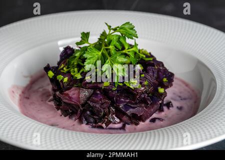 Gebratener Rotkohl in Glühwein serviert auf weißem Teller. Hintergrund: Gebratener Blaukohl, Makro. Schließen Stockfoto