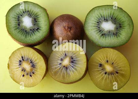 Drei in Scheiben geschnittene ​​ Kiwis auf einem gelben Schneidebrett. Zwei sind goldene Kiwis oder Actinidia chinensis, die andere ist ein grünes oder Actinidia deliciosa. Stockfoto