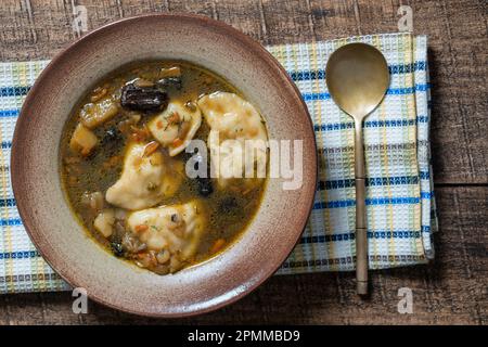 Pilzsuppenteller mit Porcini-Pilzen, Knödeln, Kartoffeln, Karotten, Zwiebeln, Frischer grüner Dill und Pfeffer auf schwarzem Hintergrund, Nahaufnahme, Draufsicht Stockfoto