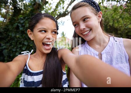 Du bist fantastisch... Nein, du bist toll. Zwei junge Freundinnen machen draußen ein Selfie. Stockfoto