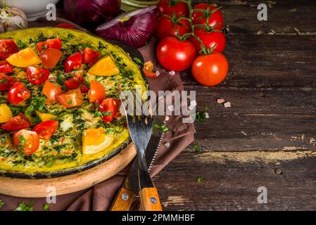 Hausgemachte rustikale Frittata. Frittata mit Spinat, Käse und Tomaten in Pfanne. Holzhintergrund mit Gemüse kopieren Raum Stockfoto