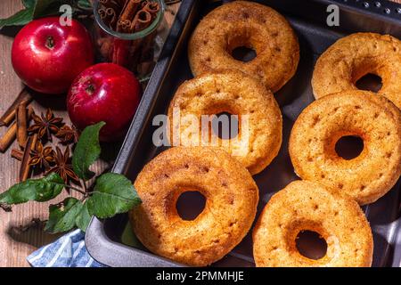 Traditionelle leckere, verzehrfertige Apfelmost-Donuts. Hausgemachte gebackene Apfel-Zimt-Donuts mit Apfelkuchen-Krümel und Gewürzen, serviert auf Holztischkopie Stockfoto