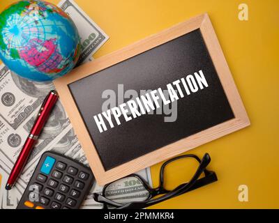 Holzbrett, Taschenrechner, Erdkugel und Banknoten mit dem Wort HYPERINFLATION auf gelbem Hintergrund. Stockfoto