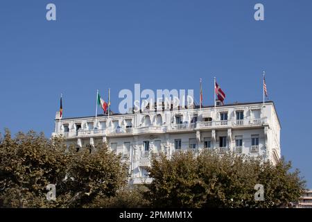 Das Hotel ist herrlich am Strand von Cannes an der Cote d'Azur. Das weiße Schild und die bemalte Fassade heben sich unter einem wolkenlosen blauen Himmel hervor. Stockfoto