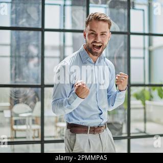 Porträt eines jungen Geschäftsmannes in einem blauen Hemd, der seine Fäuste schüttelt und seinen Erfolg feiert Stockfoto