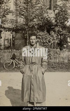 Rom, Italien Mai 1951: Ein stilvoller junger Mann in einem langen Mantel und ein wunderschönes Mädchen, das auf dem Rasen sitzt und eine klassische 1950er-Ästhetik hervorruft. Stockfoto