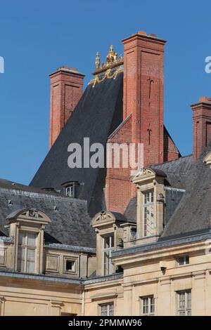 Fontainebleau Palast: Die Ziegelschornsteine, das steile Schieferziegeldach und die goldene Akroterie auf dem mittelalterlichen Schornstein vom Place de la Fontaine aus gesehen Stockfoto