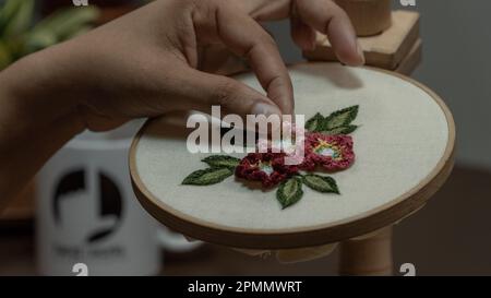 Frauenhände, die eine Blume auf einen Holzkorb sticken. Stockfoto