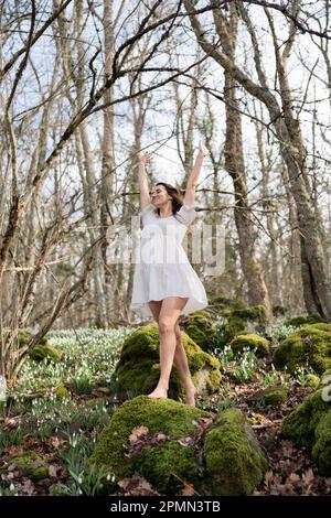 Schneeglöckchen galanthus-Frau. Sie steht in einem weißen Kleid auf einer Wiese mit Schneeglöckchen in einem Frühlingswald Stockfoto