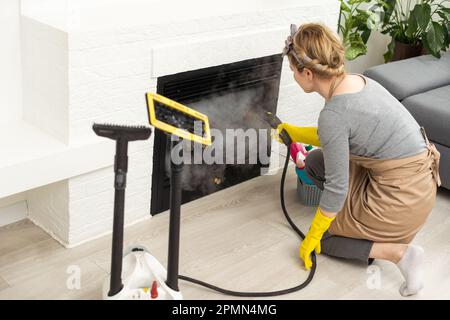 Die Frau wäscht den Boden im Zimmer mit einem weißen Dampfreiniger, einem nassen Hochdruckdampf. Reinigung der Wohnung. Wir töten Mikroben Stockfoto