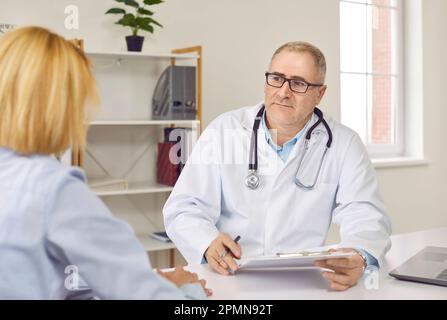 Senior männlicher Arzt hört auf seine weibliche Patientin während der ärztlichen Beratung Stockfoto