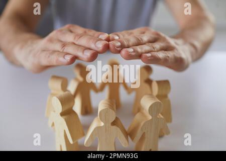 Männerhände, die ein Team von Menschen aus Holz bedecken und schützen Stockfoto