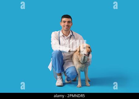 Männlicher Tierarzt mit niedlichem Labrador-Hund auf blauem Hintergrund Stockfoto